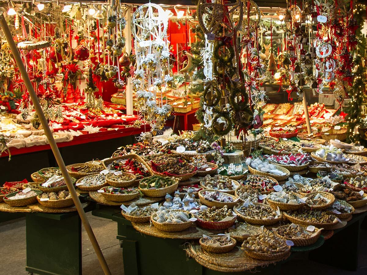 Festlicher Weihnachtsmarktstand mit Körben voller handgemachter Deko, Nüssen und Gewürzen, im Hintergrund weitere Ornamente.