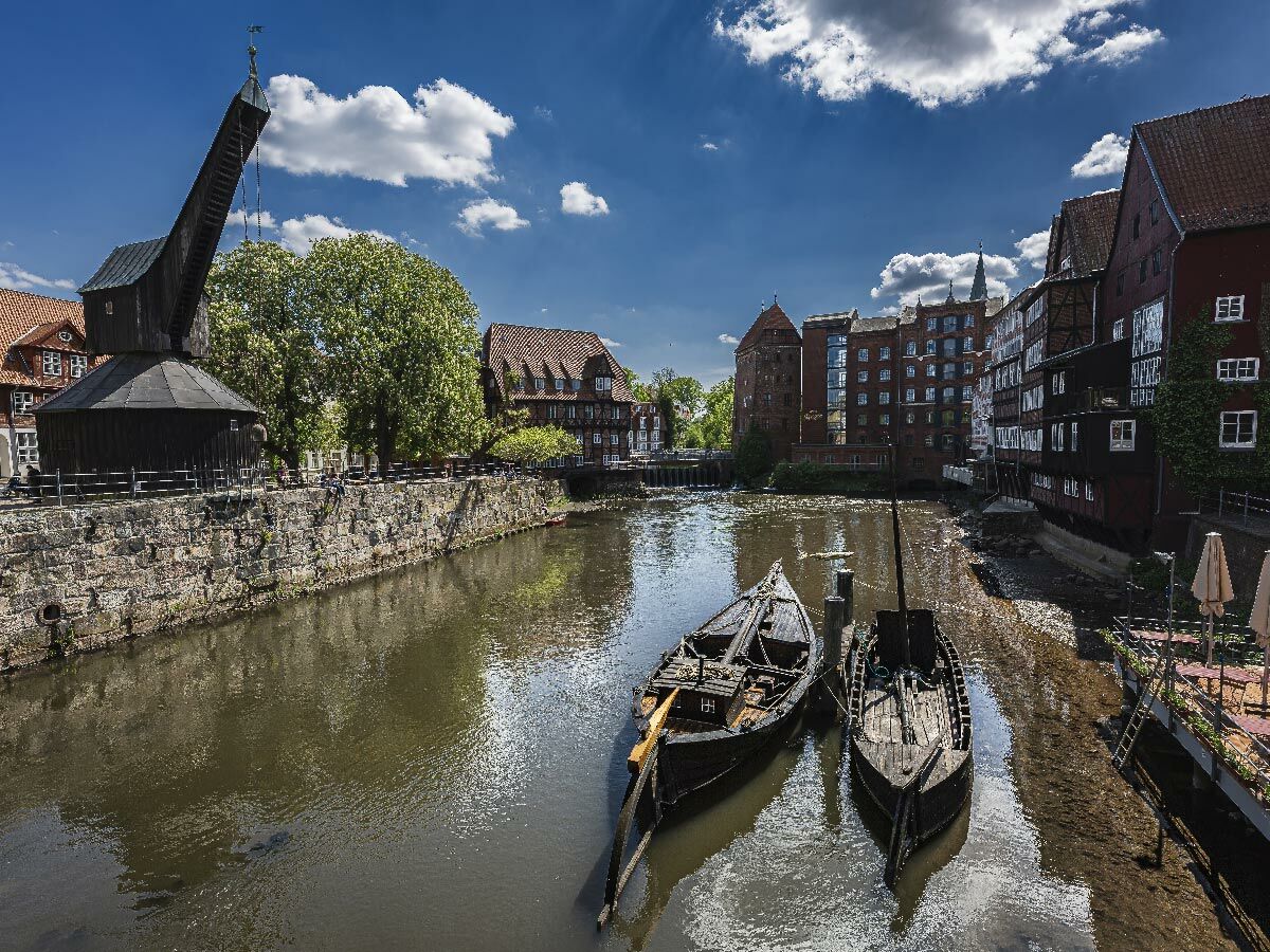 Historischer Holzkran am Lüneburger Kanal mit alten Giebelhäusern, traditionellen Booten und blauem Himmel.