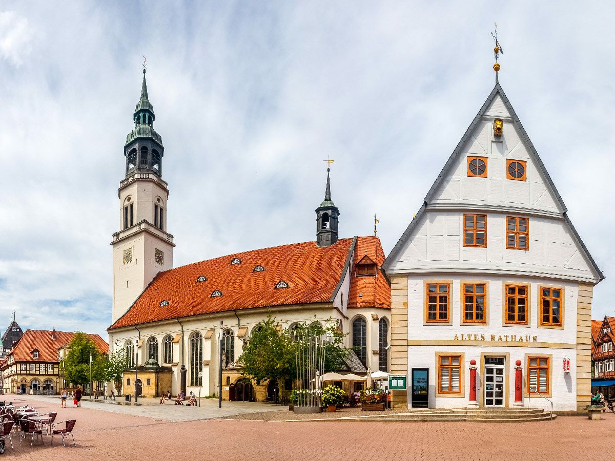 Blick auf einen belebten historischen Marktplatz mit dem Alten Rathaus, einer Kirche und Fachwerkhäusern unter bewölktem Himmel.