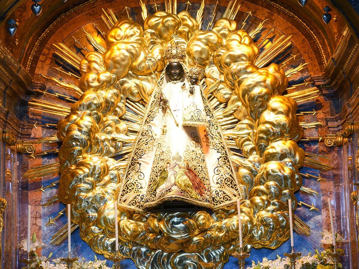 Schwarze Madonna mit Kind in Gold und Weiß, umgeben von goldenen Strahlen und Wolken in einem Kirchenschrein.