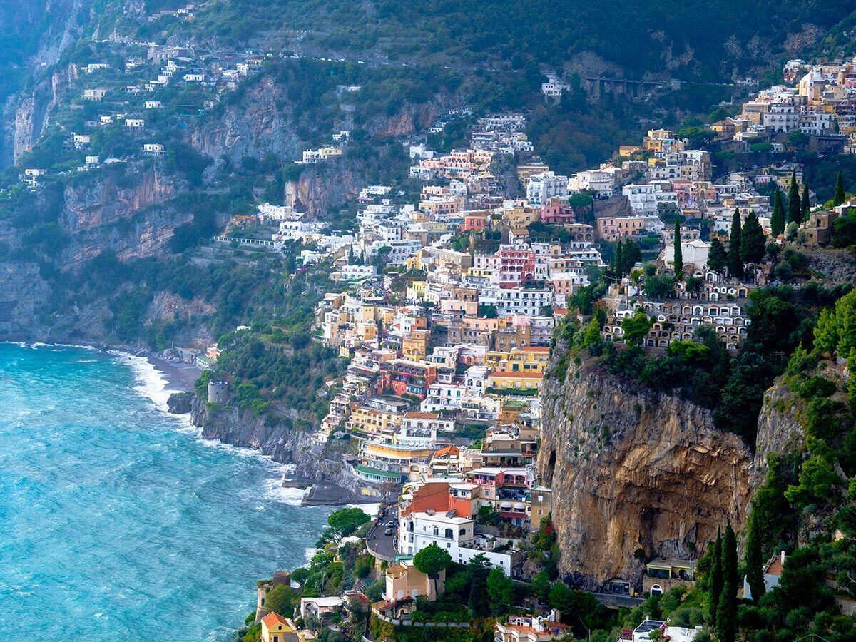 Panoramablick auf die italienische Küstenstadt Positano mit bunten Häusern an steilen Klippen und dem blauen Mittelmeer.