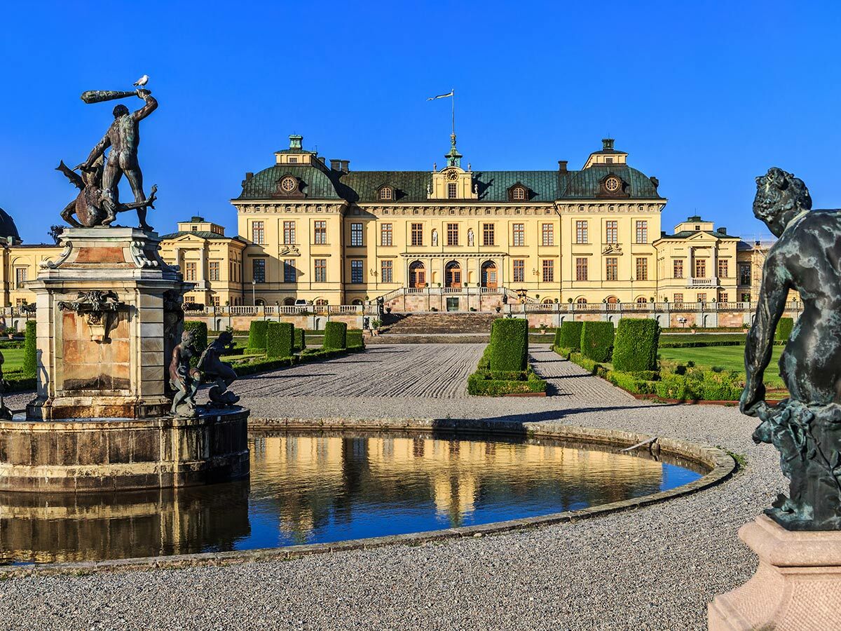 Drottningholm Schloss in Schweden mit klassizistischen Statuen, Brunnen, Reflektionen und gepflegten Gärten unter blauem Himmel.