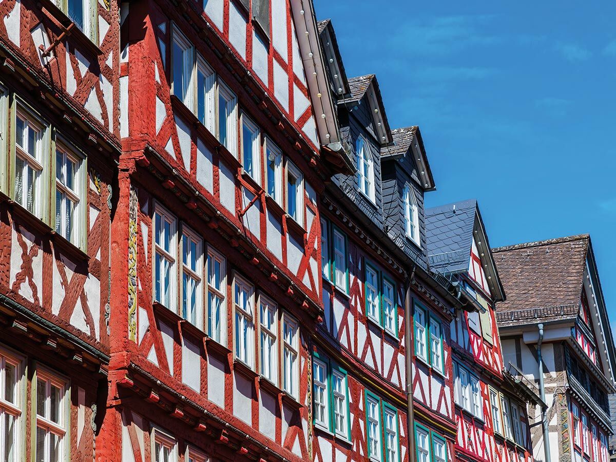 Reihe traditioneller Fachwerkhäuser mit roten Holzbalken, weißen Wänden und grünen Fenstern unter blauem Himmel, typisch deutsch.