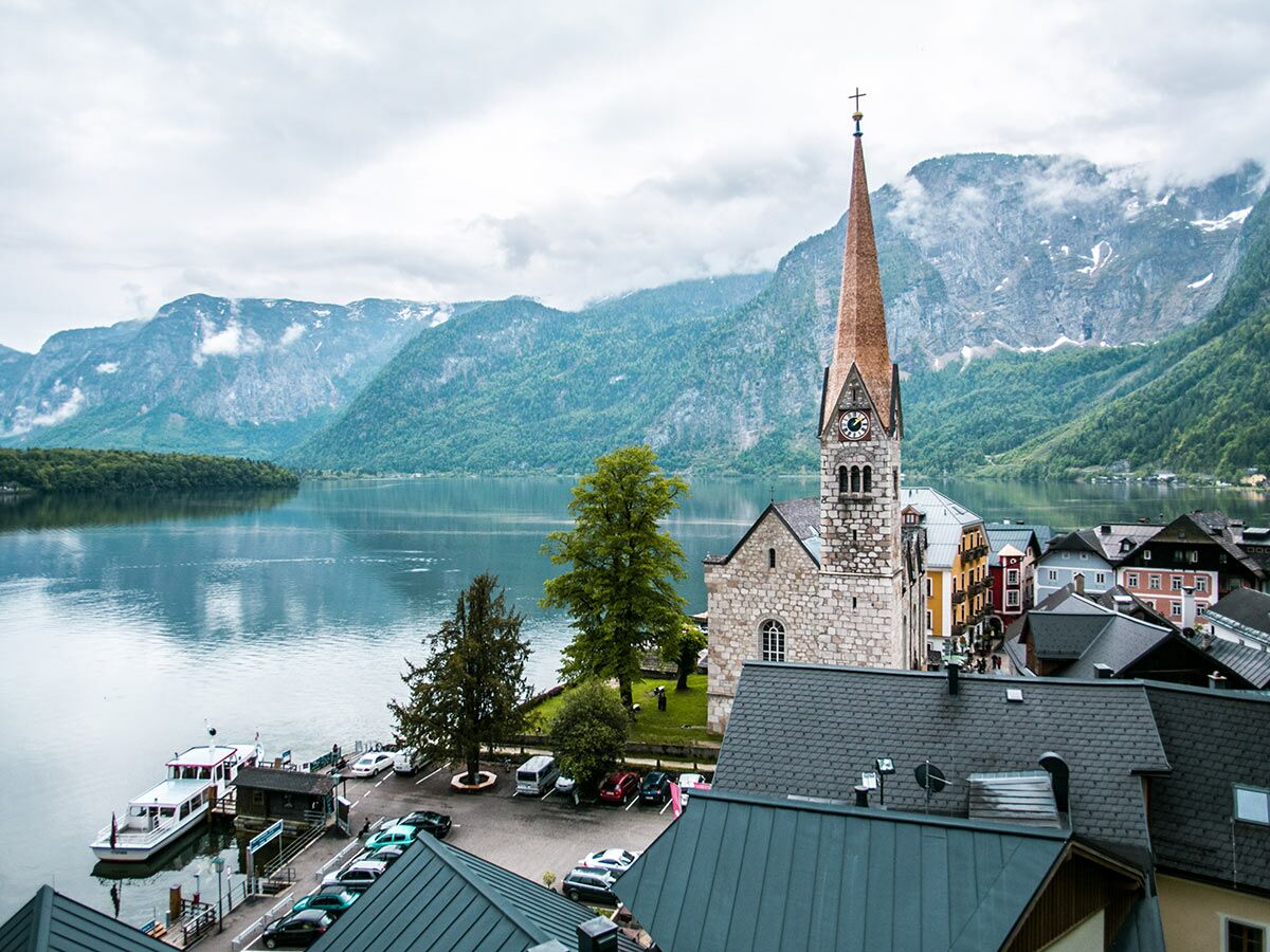 Panoramablick auf Hallstatt mit der Lutherischen Kirche, Hallstätter See und Alpenlandschaft unter bewölktem Himmel.