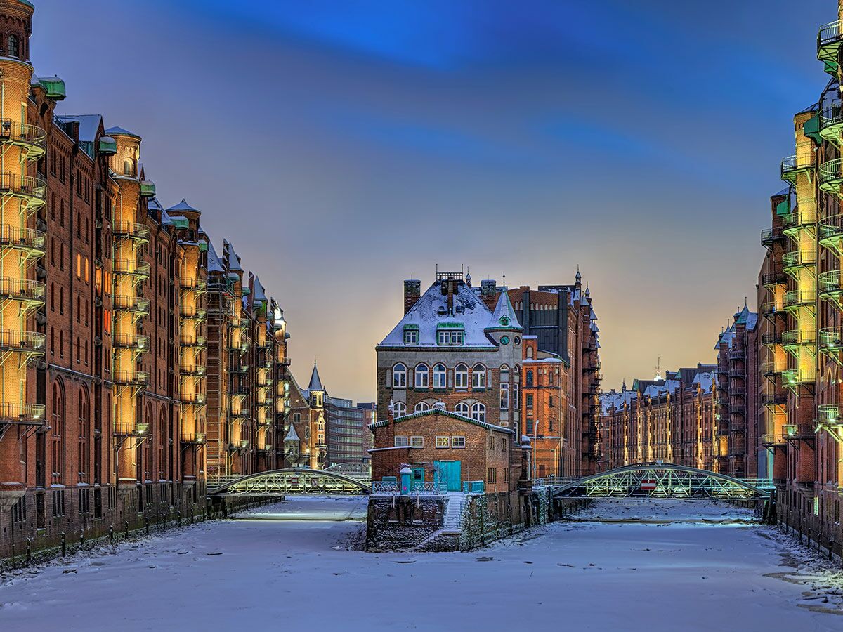 Historische Speicherstadt Hamburg im Winter bei Sonnenuntergang, beleuchtete Backsteingebäude entlang eines verschneiten Kanals.