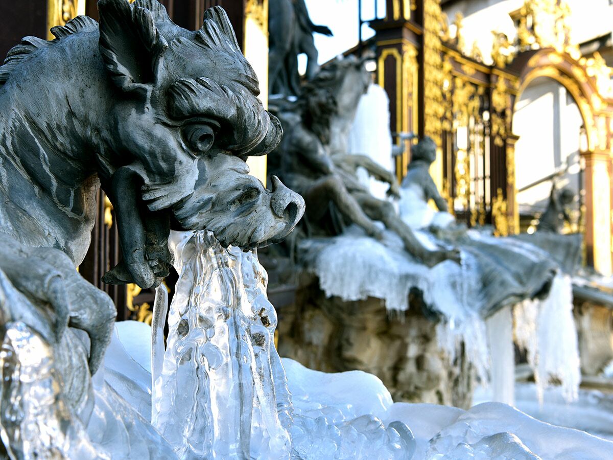 Detailansicht eines gefrorenen Brunnens mit einer steinernen Fabeltier-Skulptur und glitzernden Eiszapfen.