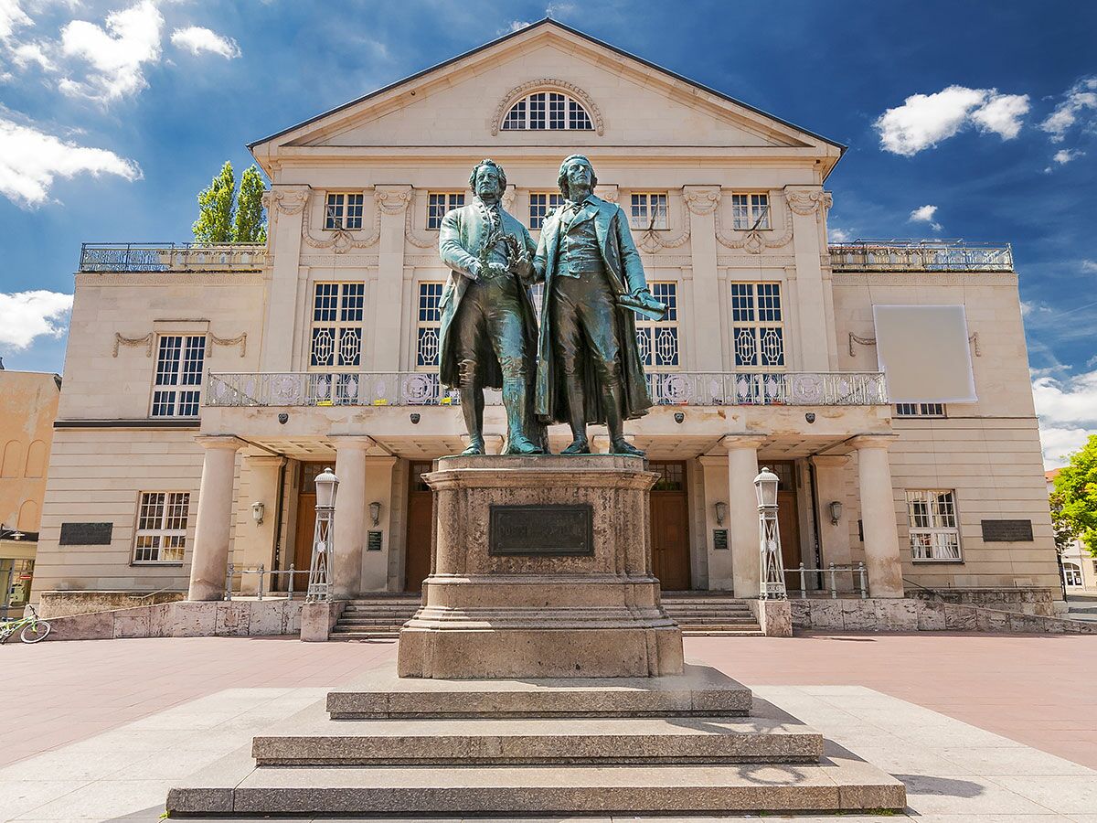 Goethe-Schiller-Denkmal vor dem Deutschen Nationaltheater in Weimar bei blauem Himmel.