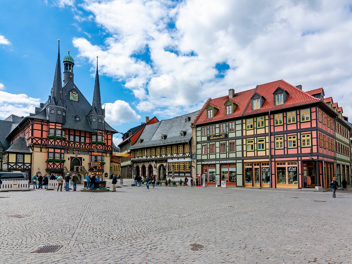Historischer Marktplatz Wernigerode mit Rathaus, bunten Fachwerkhäusern und Menschen unter blauem Himmel.