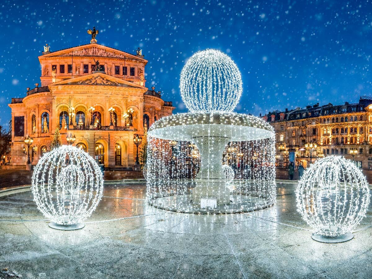 Festlich beleuchtete Alte Oper Frankfurt im Schnee mit funkelndem Brunnen und großen Lichtkugeln am Abend.