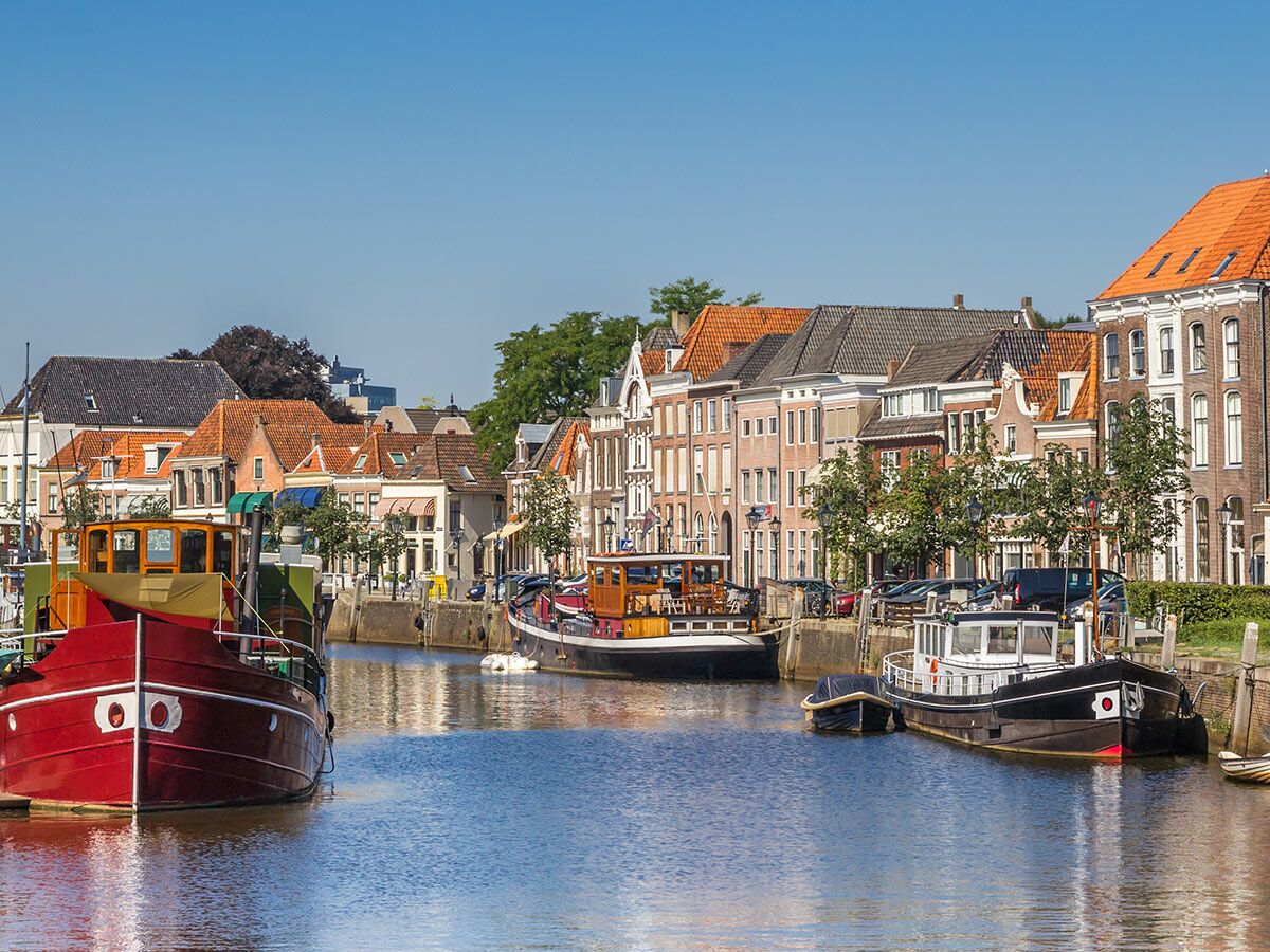 Malerischer Kanal mit historischen Gebäuden und bunten Booten an einem sonnigen Tag in einer niederländischen Stadt.