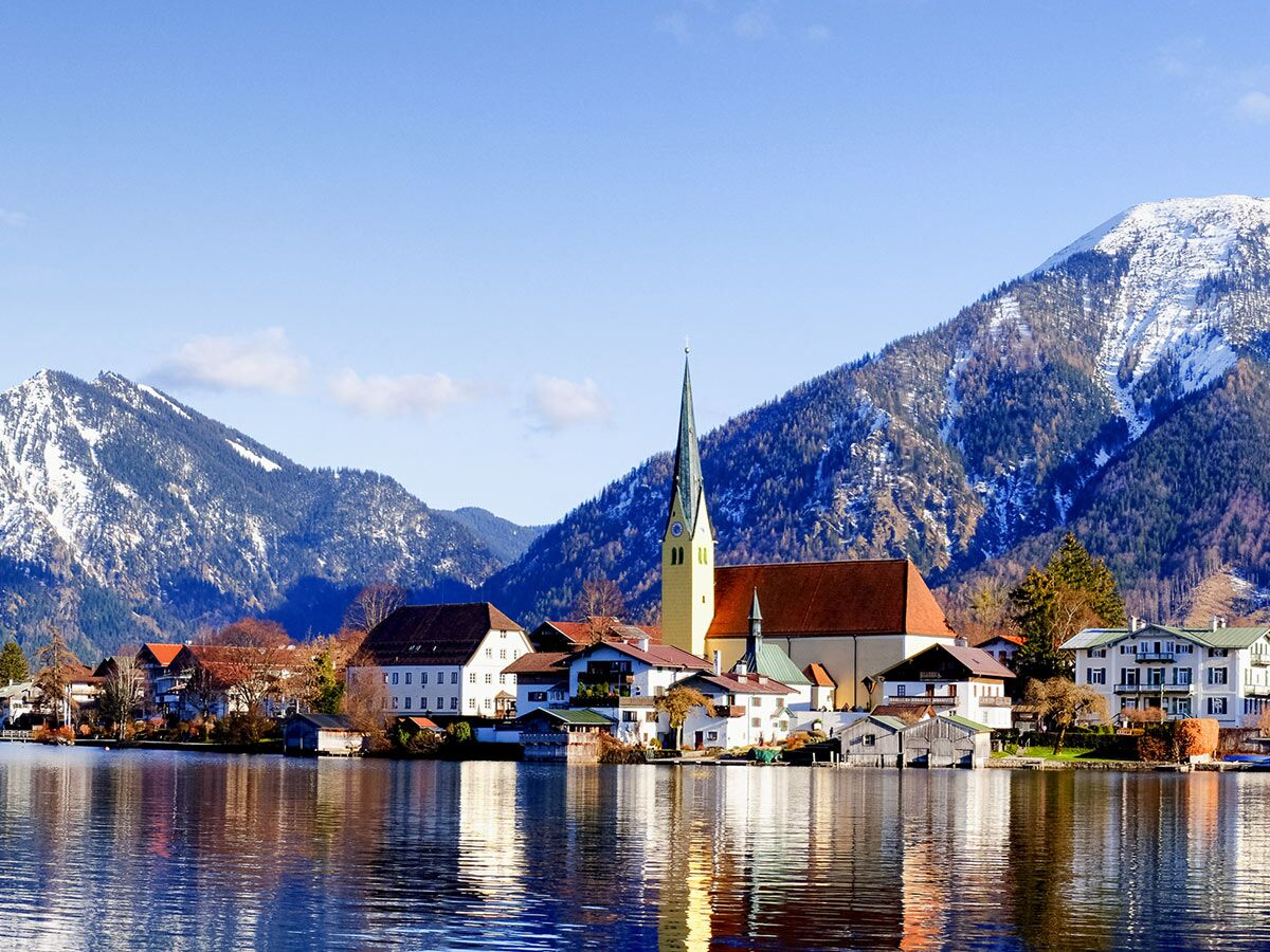 Malerisches Rottach-Egern am Tegernsee mit Kirche St. Laurentius und schneebedeckten Alpen im Winter.