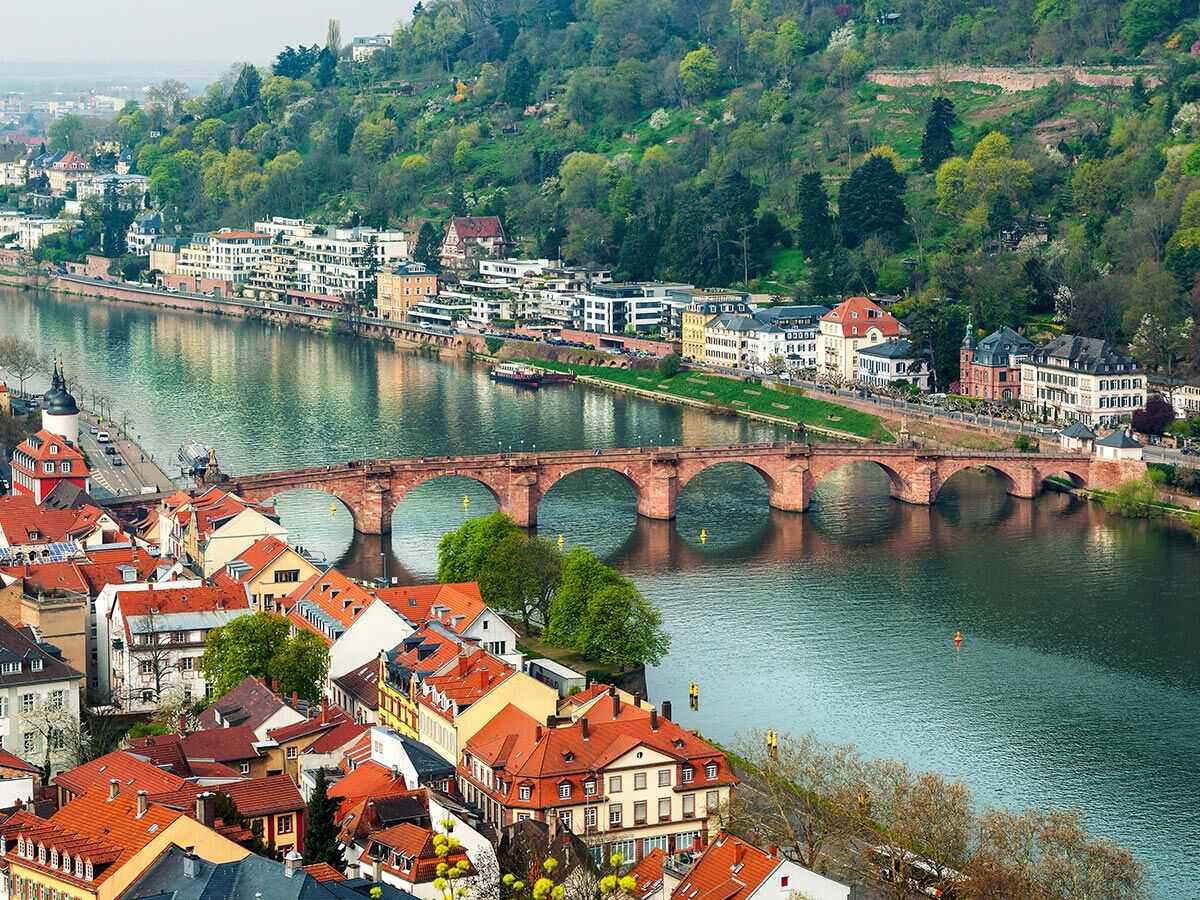Panoramablick auf Heidelberg mit der Alten Brücke über den Neckar, historischen Gebäuden und grünen Hügeln im Frühling.