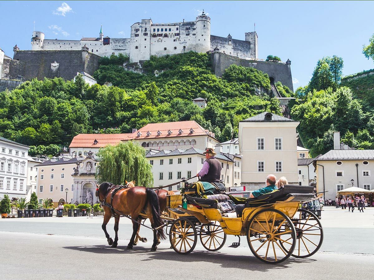 Historische Kutschfahrt in Salzburg mit der Festung Hohensalzburg und Touristen vor barocken Gebäuden im Sommer.