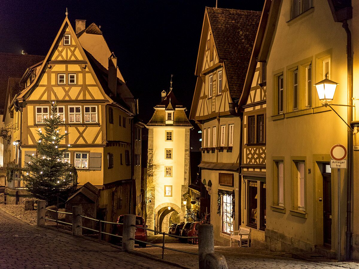 Historische Gasse in Rothenburg ob der Tauber bei Nacht mit Fachwerkhäusern, beleuchtetem Weihnachtsbaum und Torbogen.
