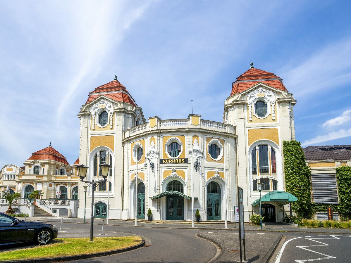 Großes, historisches Kurhaus-Gebäude mit gelb-weißer Fassade, roten Dächern und Verzierungen unter blauem Himmel.