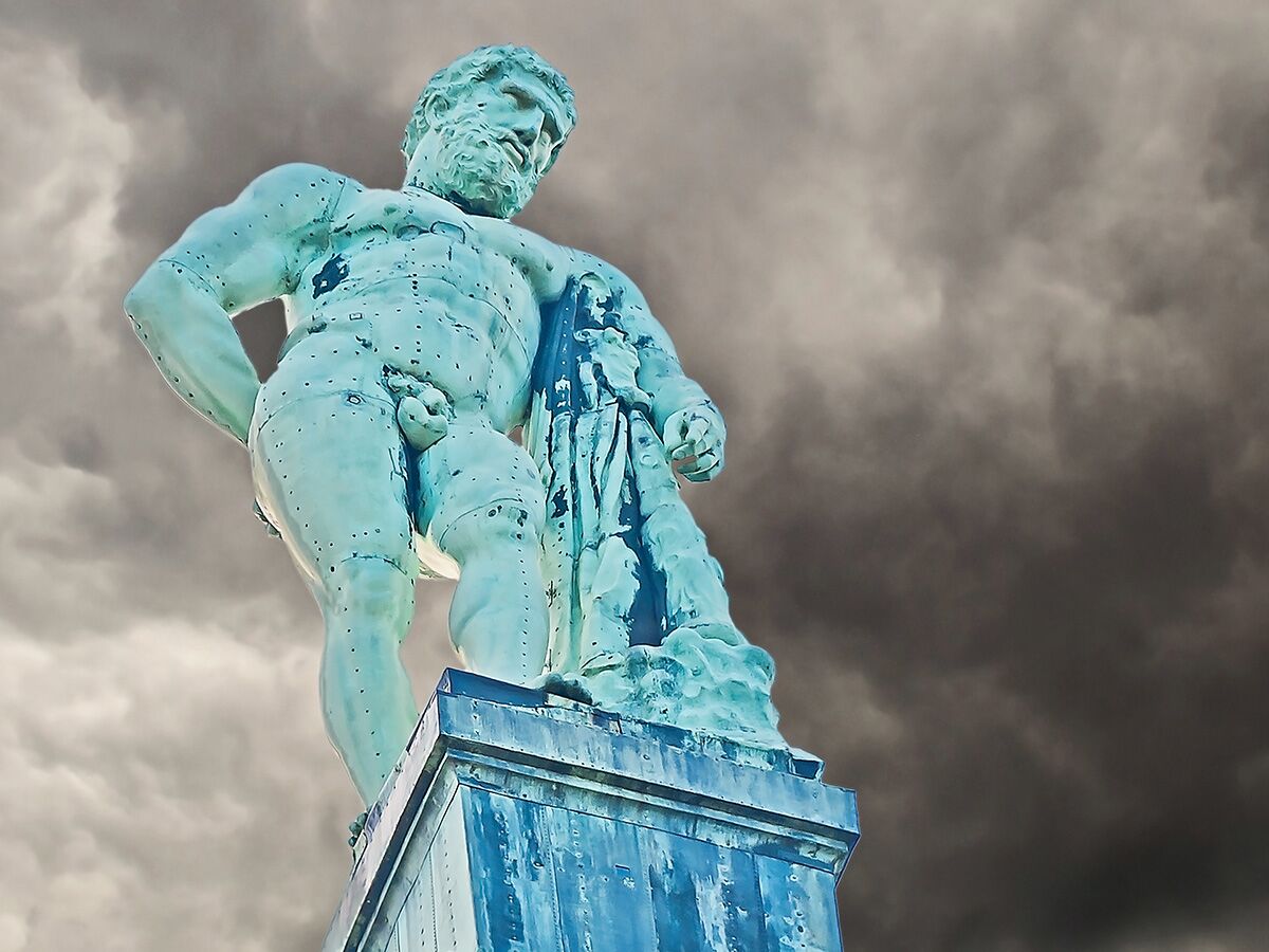 Große blaugrüne Bronze-Statue eines muskulösen Mannes, Herkules, vor dramatisch dunklem, bewölktem Himmel. Der Held steht auf einem Sockel.