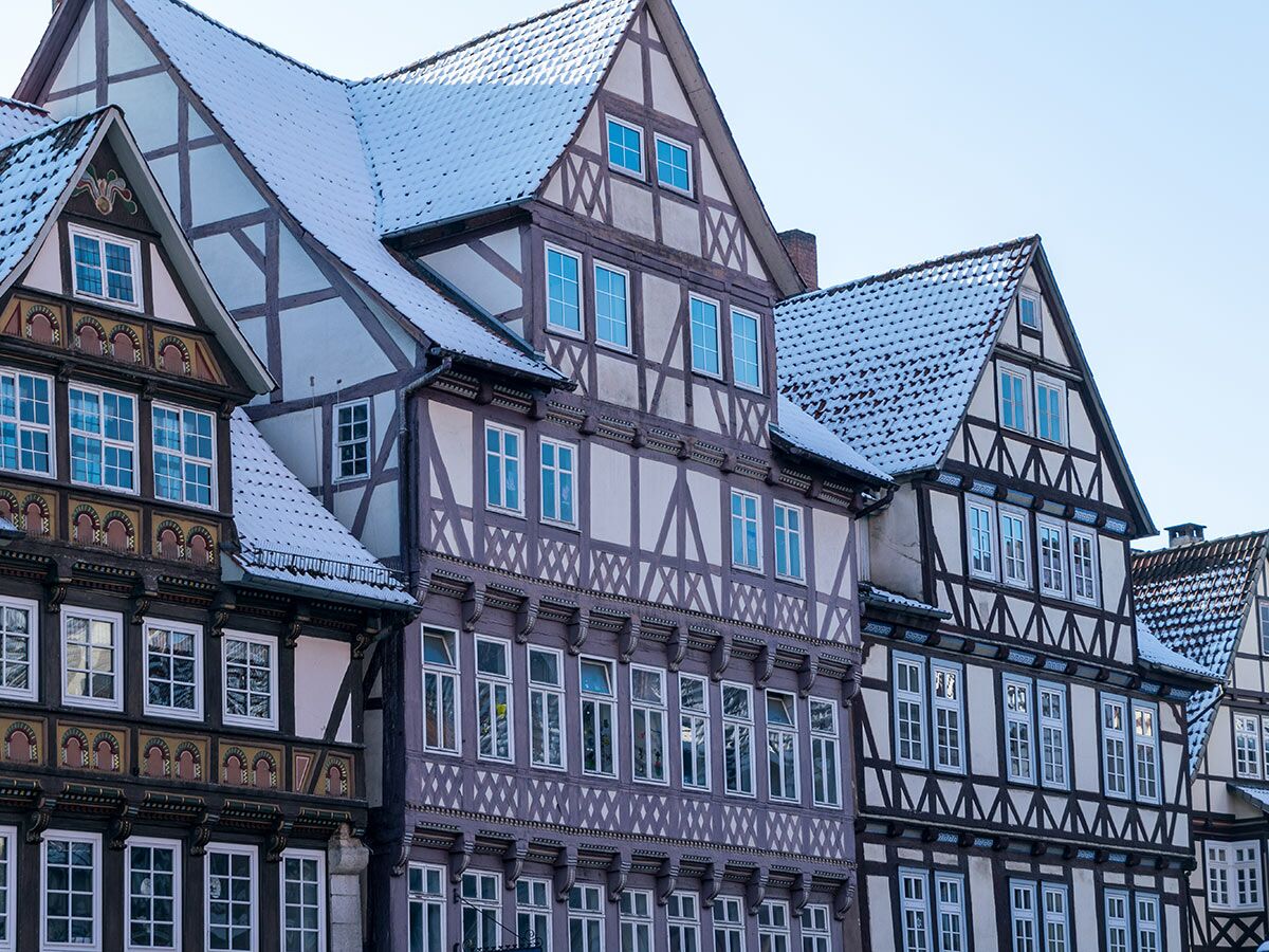 Reihe historischer Fachwerkhäuser mit schneebedeckten Dächern und hellblauen Fenstern, winterliche Szene.