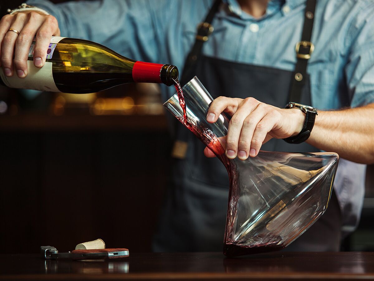 Ein Sommelier dekantiert elegant Rotwein aus einer Flasche in eine stilvolle Glaskaraffe, um das Aroma zu entfalten.