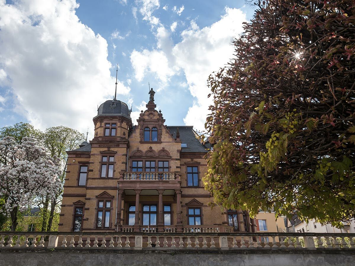 Prächtige Backsteinvilla mit Turm, Balkon und Statue, umgeben von blühenden Magnolienbäumen im Frühling.