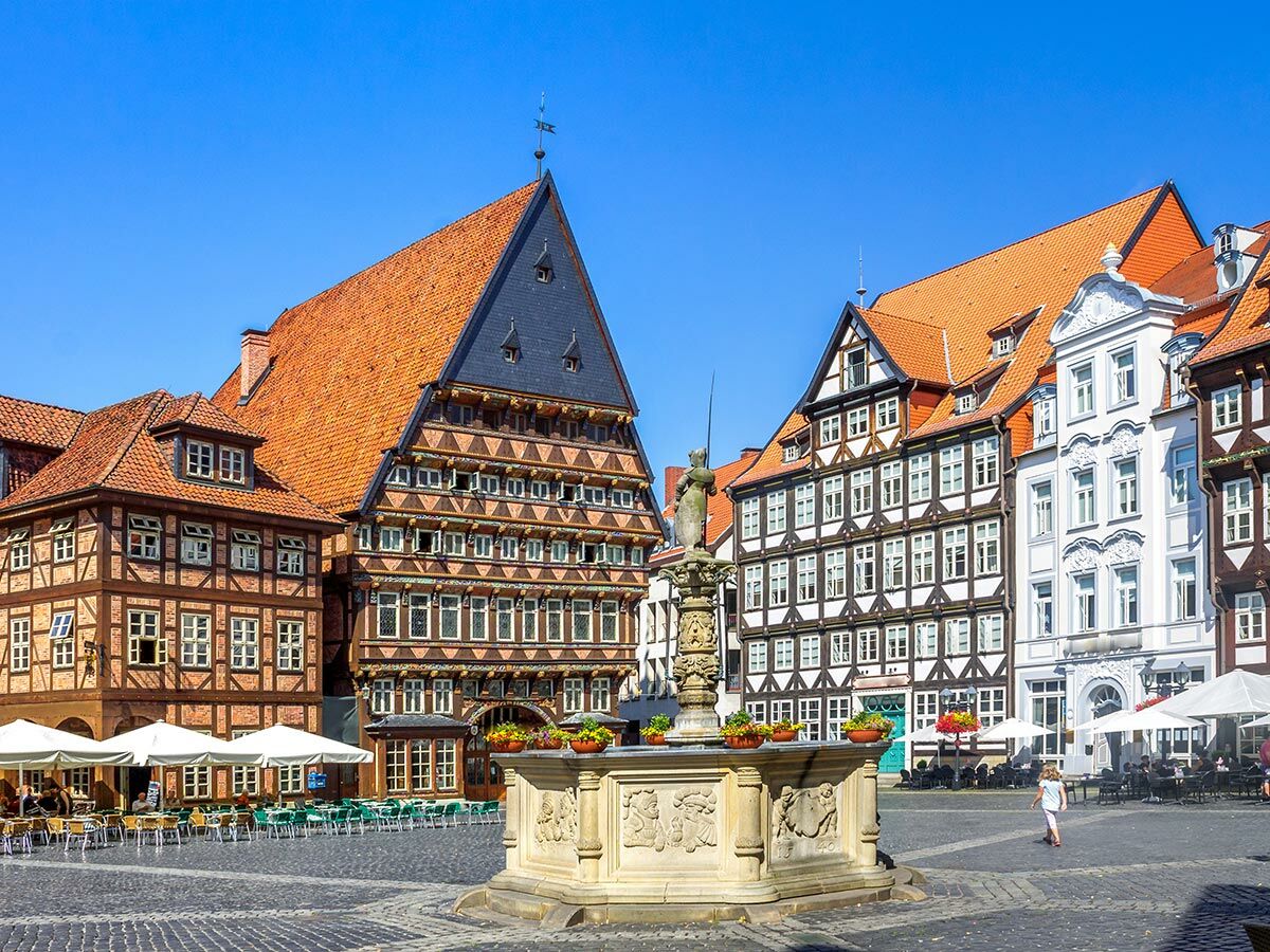 Historischer Marktplatz in Hildesheim mit prächtigen Fachwerkhäusern, dem Knochenhaueramtshaus und dem Godehardbrunnen bei Sonnenschein.