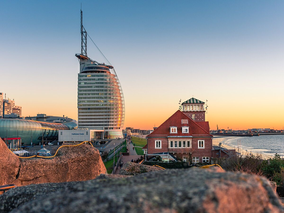 Panorama von Bremerhaven bei Sonnenuntergang mit modernem Sail City Hotel, historischem Backsteingebäude, Promenade und Hafen.