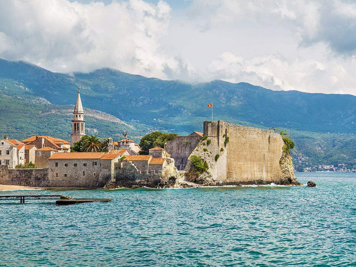 Panoramablick auf die historische Altstadt von Budva, Montenegro, mit Zitadelle, Kirche und Bergen am Meer.