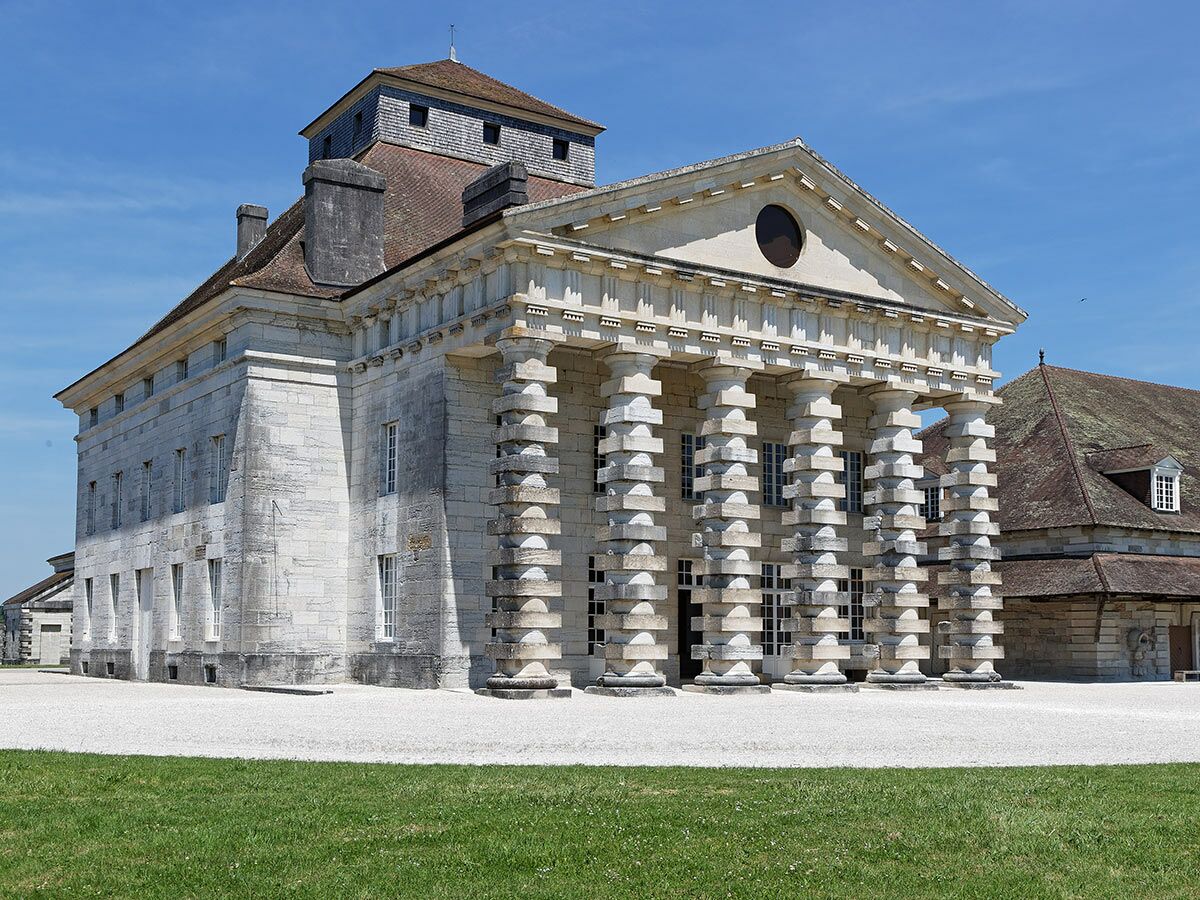 Historisches Direktorenhaus der Saline Royale Arc-et-Senans, Frankreich. Neoklassizistische Architektur mit Säulenfassade unter blauem Himmel.