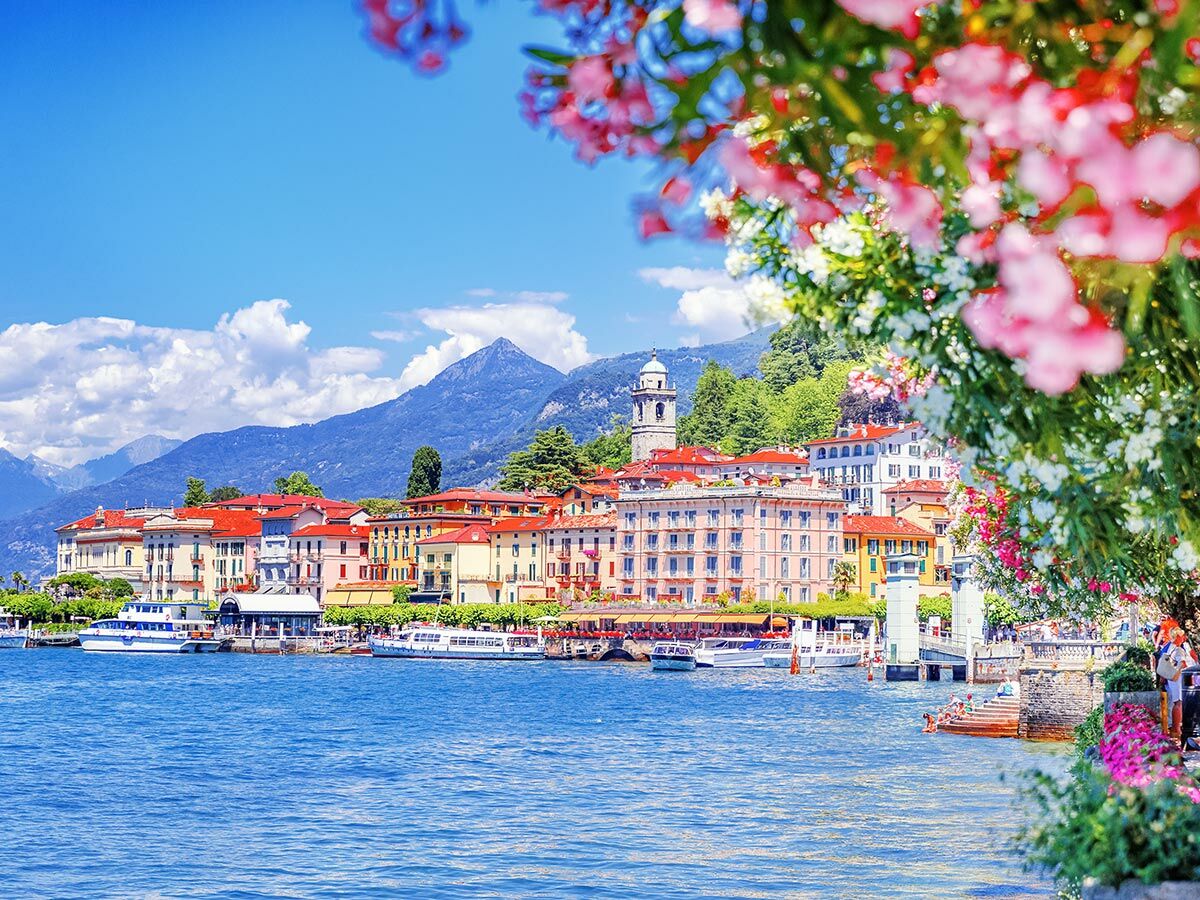 Malerisches Dorf Bellagio am Comer See, Italien, mit bunten Häusern, Bergen und Booten im Sommer, eingerahmt von Blumen.
