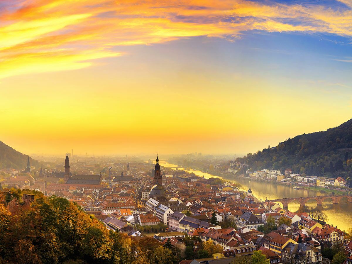 Panoramablick auf Heidelberg bei Sonnenuntergang über dem Neckar, Altstadt mit Alter Brücke und Herbstlaub.