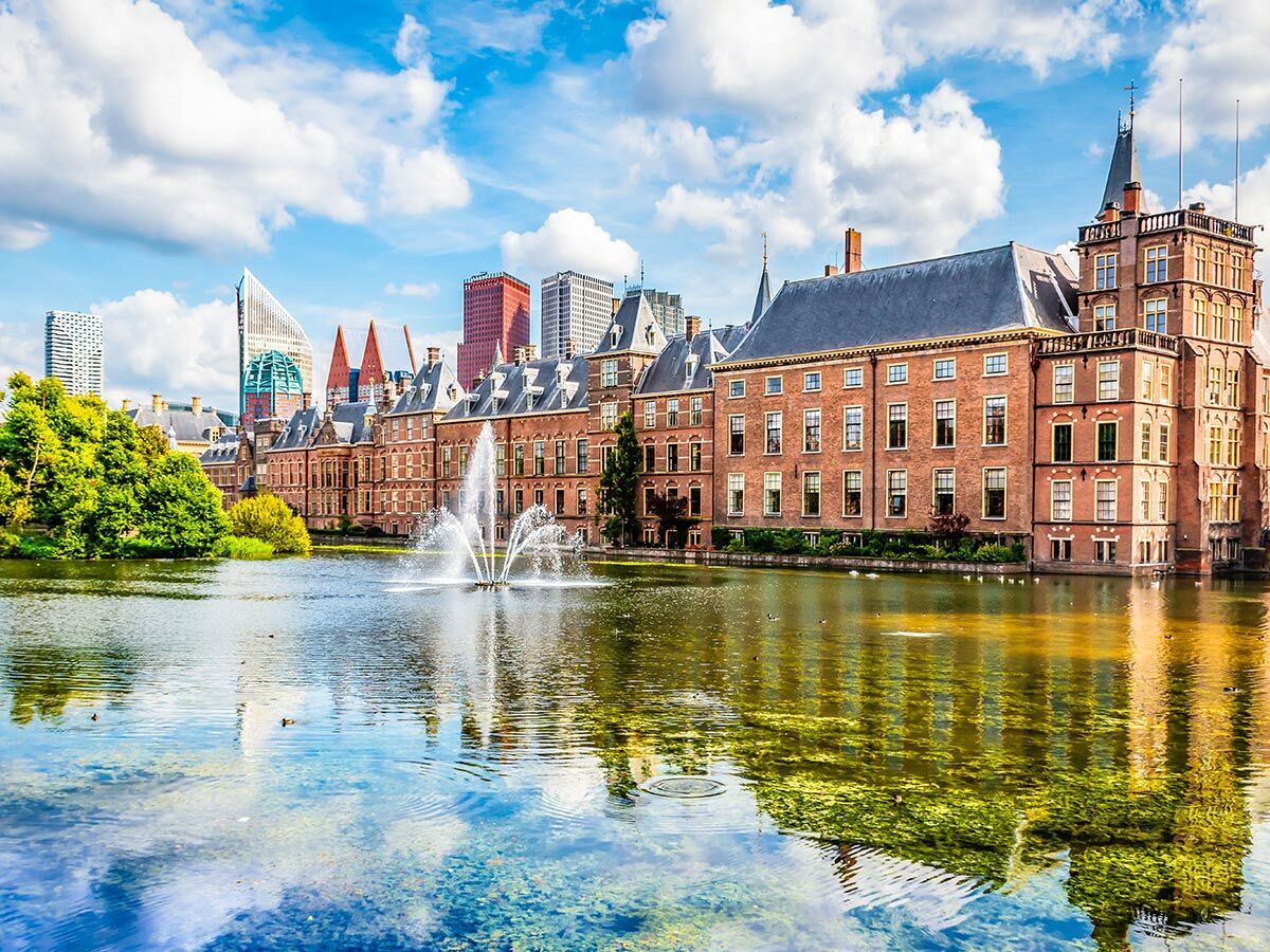 Historisches Binnenhof Parlamentsgebäude in Den Haag mit Teich, Brunnen und moderner Skyline unter blauem Himmel.