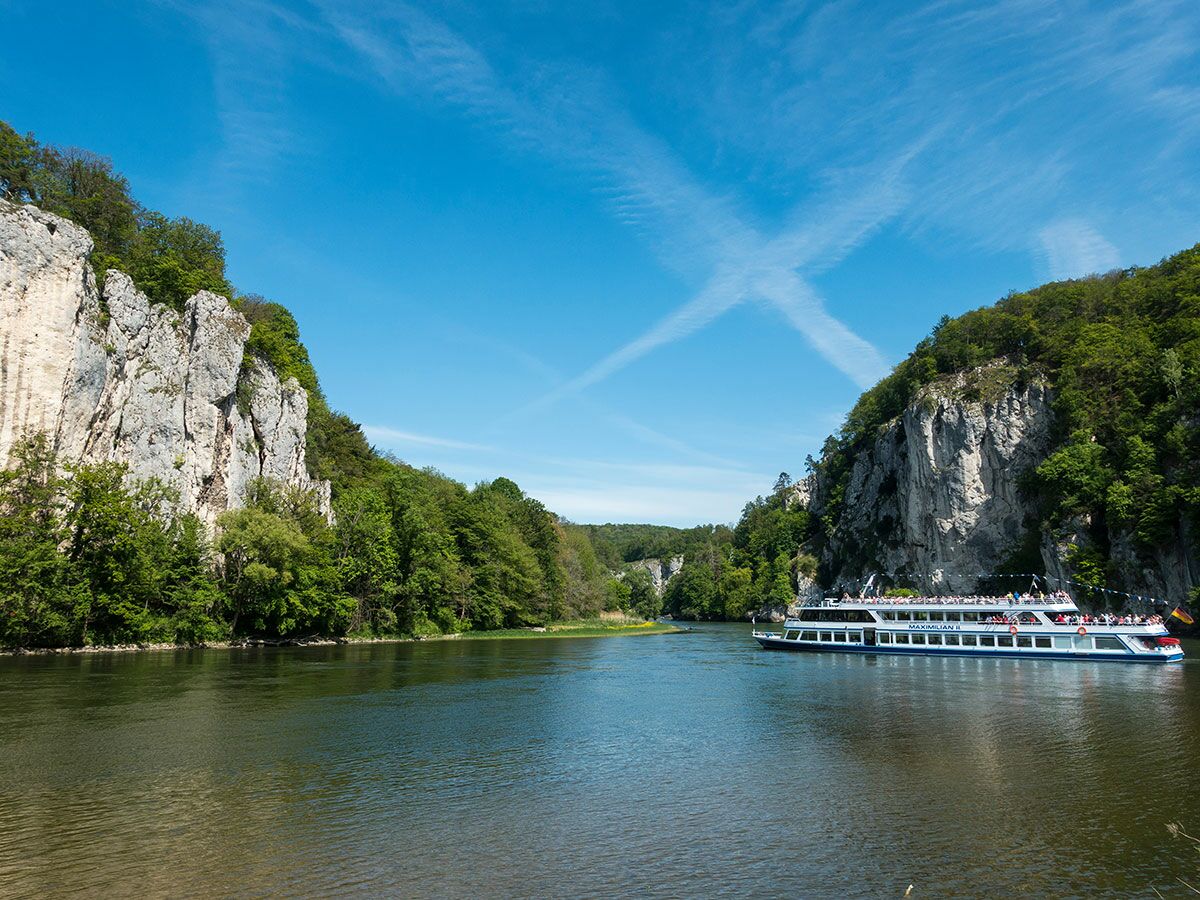 Passagierschiff "Maximilian II" fährt auf der Donau durch eine malerische Felsenschlucht mit grünen Bäumen unter blauem Himmel.