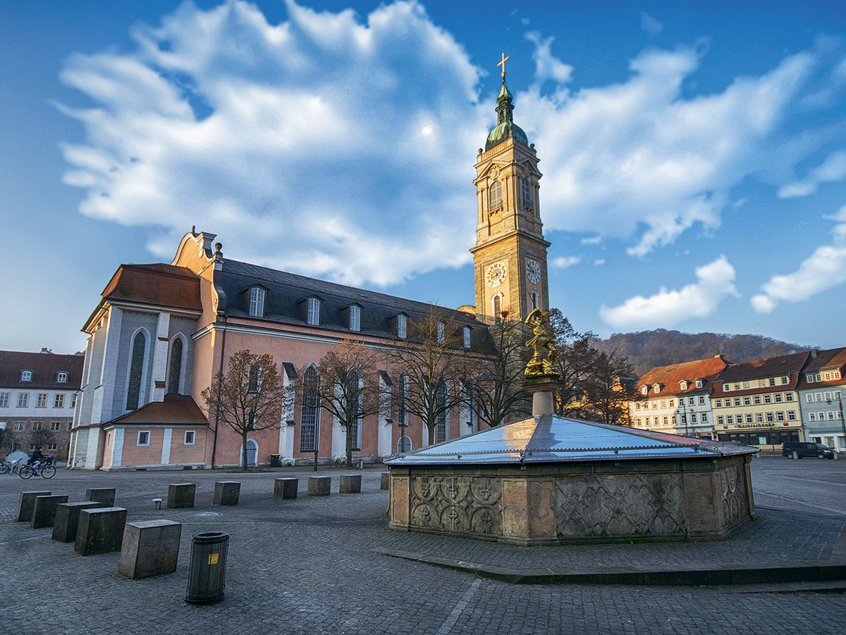 Die Stiftskirche Wertheim mit dem Georgsbrunnen auf dem Marktplatz unter blauem Himmel an einem sonnigen Tag.