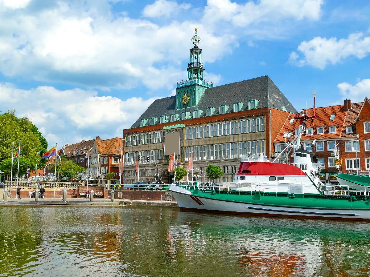 Historisches Rathaus Wilhelmshaven am Hafen mit Seenotrettungsboot, traditionellen Gebäuden und Spaziergängern unter blauem Himmel.
