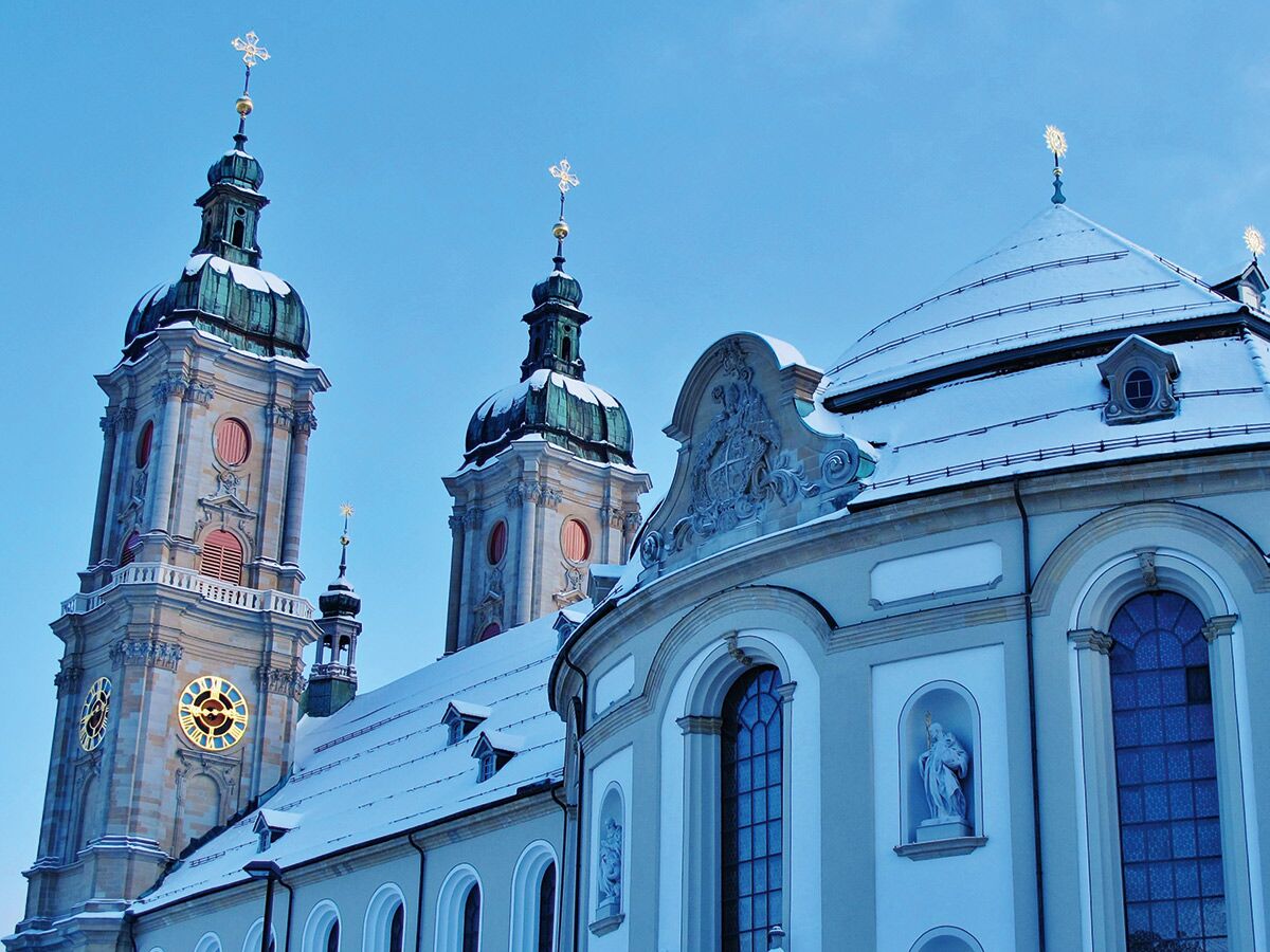Majestätische barocke Kathedrale mit schneebedeckten Türmen und Dächern unter blauem Himmel, goldene Kreuze glänzen.