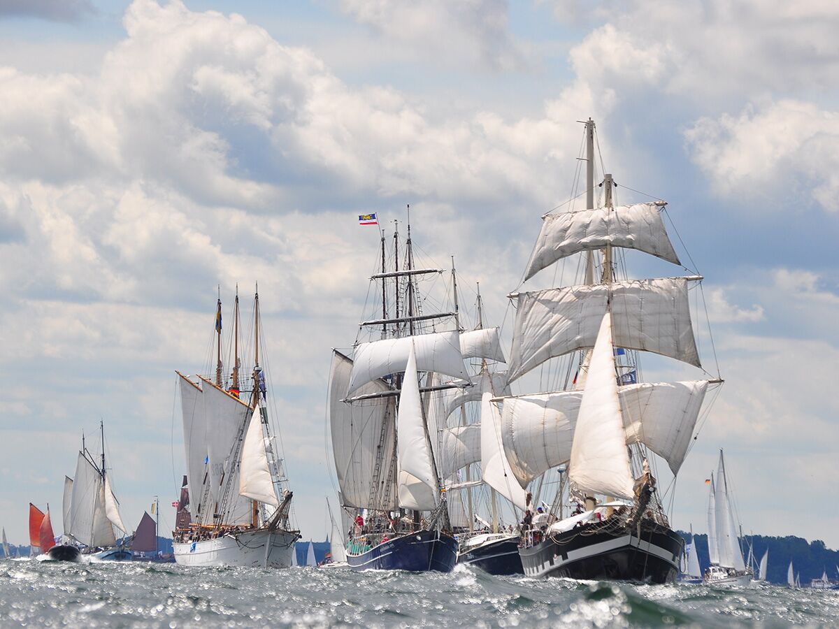 Beeindruckende Flotte von Großseglern und Segelbooten nimmt an einer Regatta auf dem weiten, welligen Meer unter bewölktem Himmel teil.