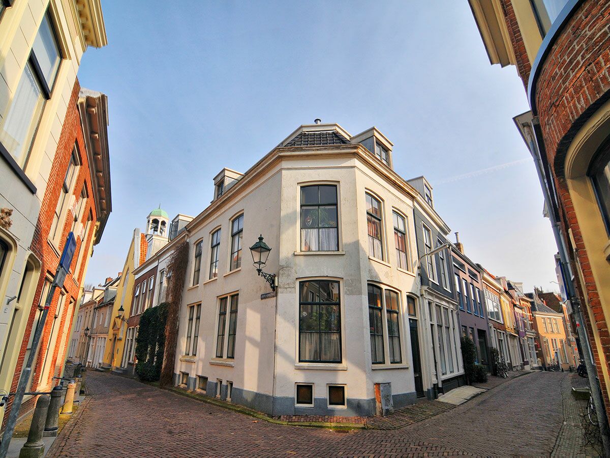 Malerische Gasse mit historischen Gebäuden und Kopfsteinpflaster in einer niederländischen Altstadt, Glockenturm im Hintergrund.