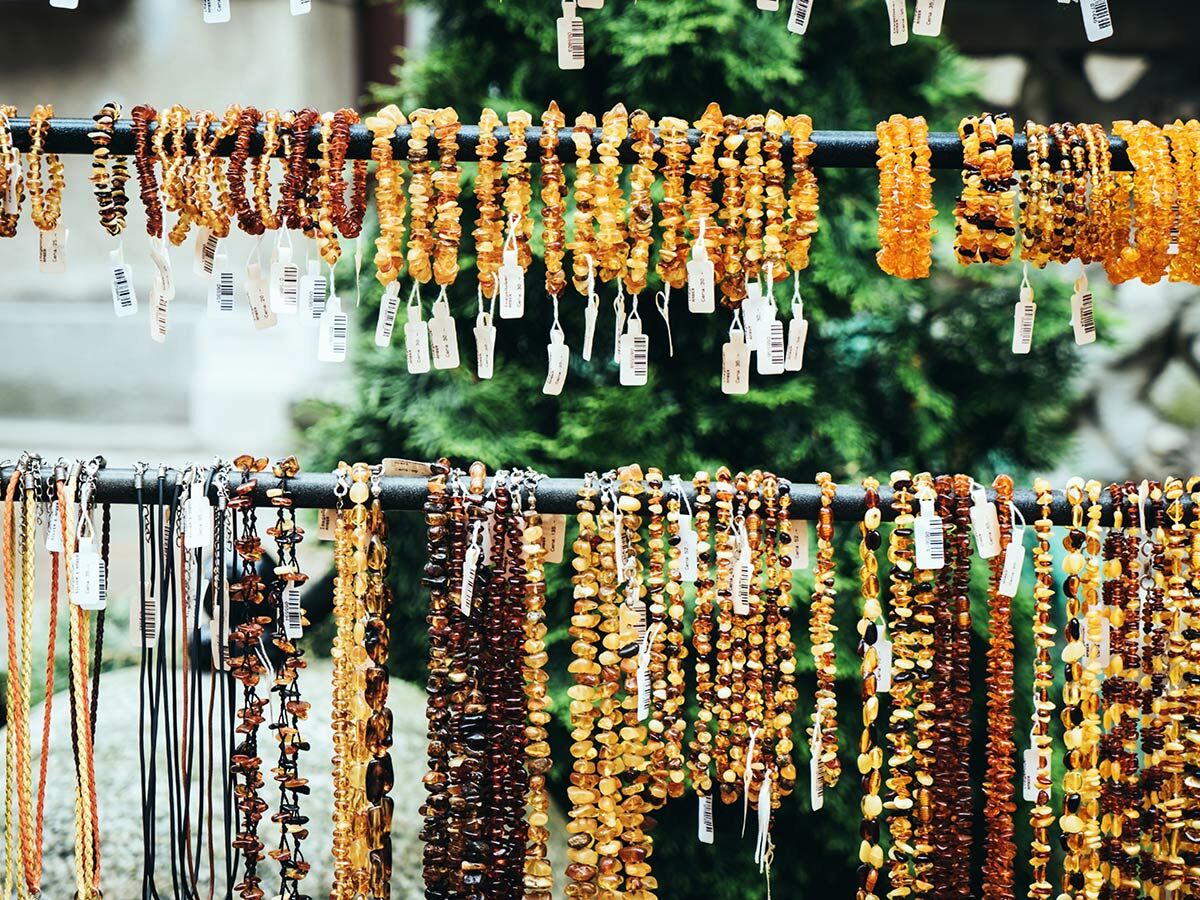 Reihen von Bernsteinketten und -armbändern in verschiedenen Gelb- und Brauntönen auf einem Marktstand vor Grün.