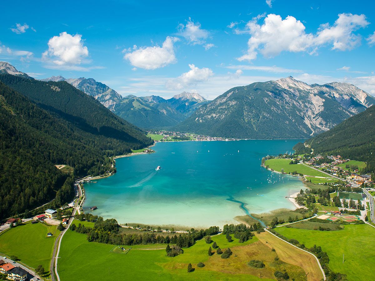 Luftaufnahme des Achensees in Tirol mit türkisblauem Wasser, grünen Ufern, umliegenden Bergen und Dörfern unter blauem Himmel.