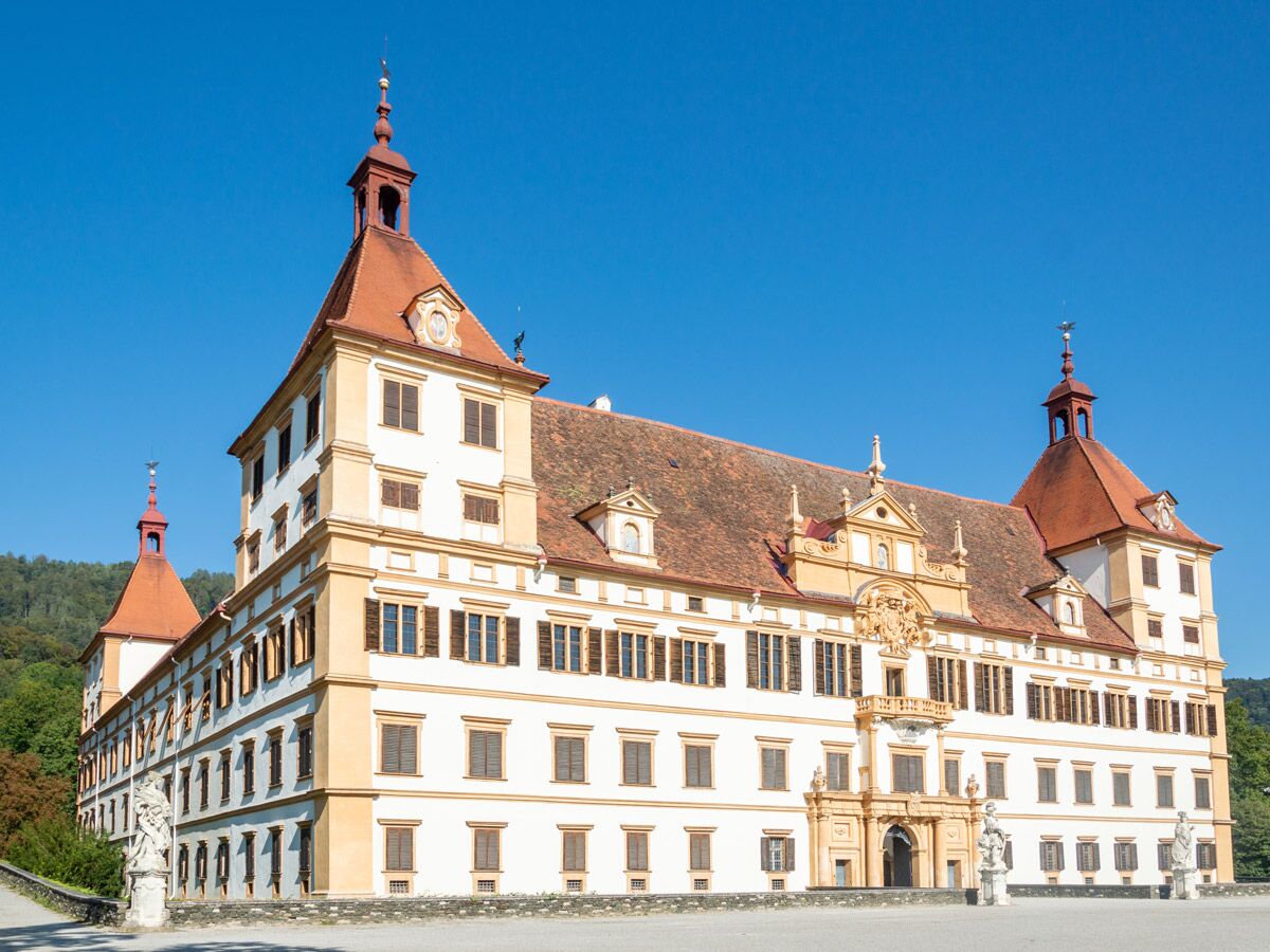 Majestätisches Schloss Eggenberg mit roten Dächern und weiß-gelber Fassade unter blauem Himmel.