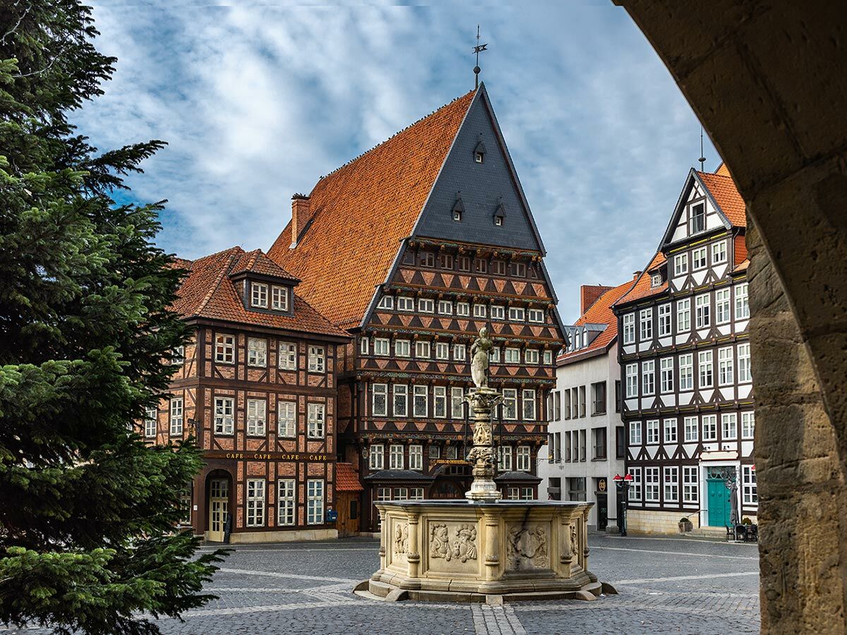 Historischer Marktplatz in Hildesheim, Deutschland, mit dem Knochenhaueramtshaus, Fachwerkhäusern und Brunnen unter blauem Himmel.