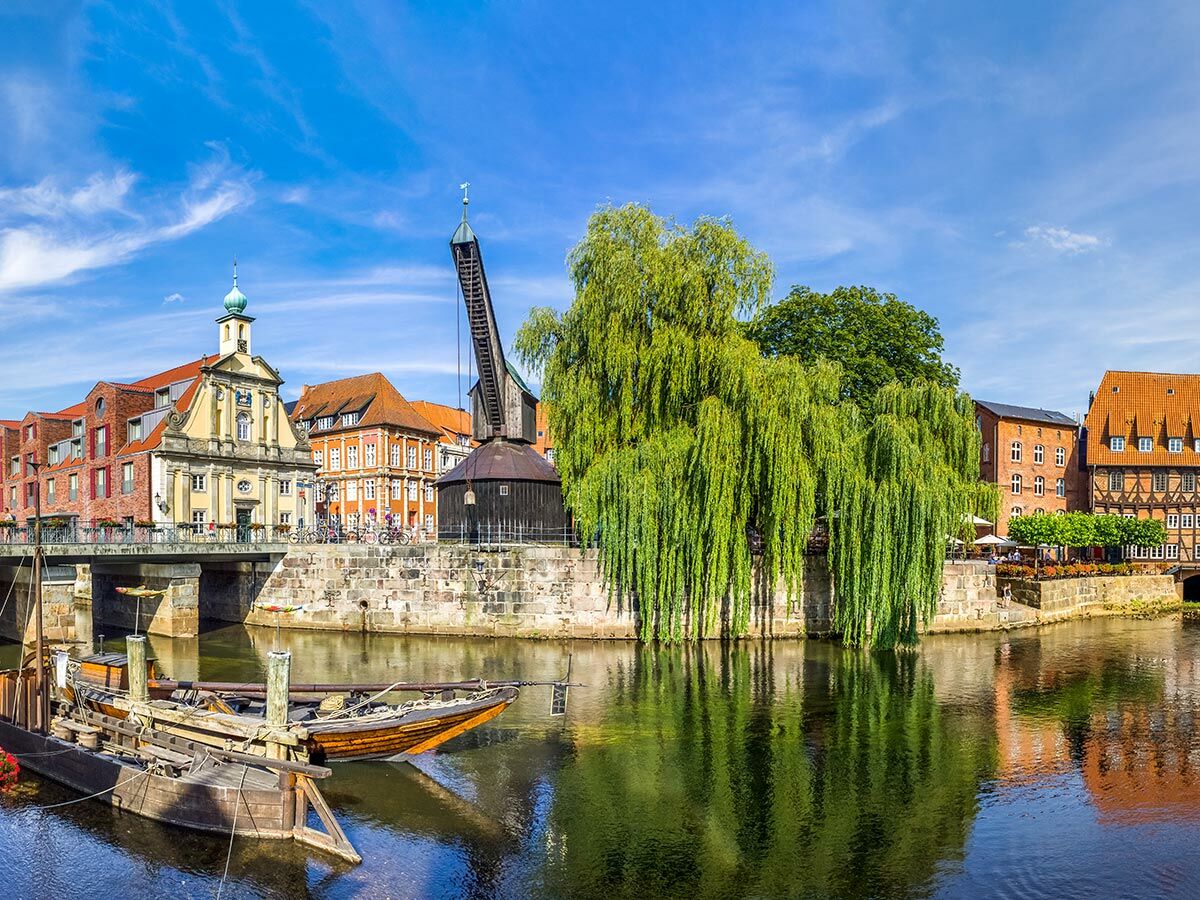 Historische Altstadt Lüneburg mit Altem Kran, Gebäuden, Brücke, Booten und Weidenbaum am Fluss Ilmenau.