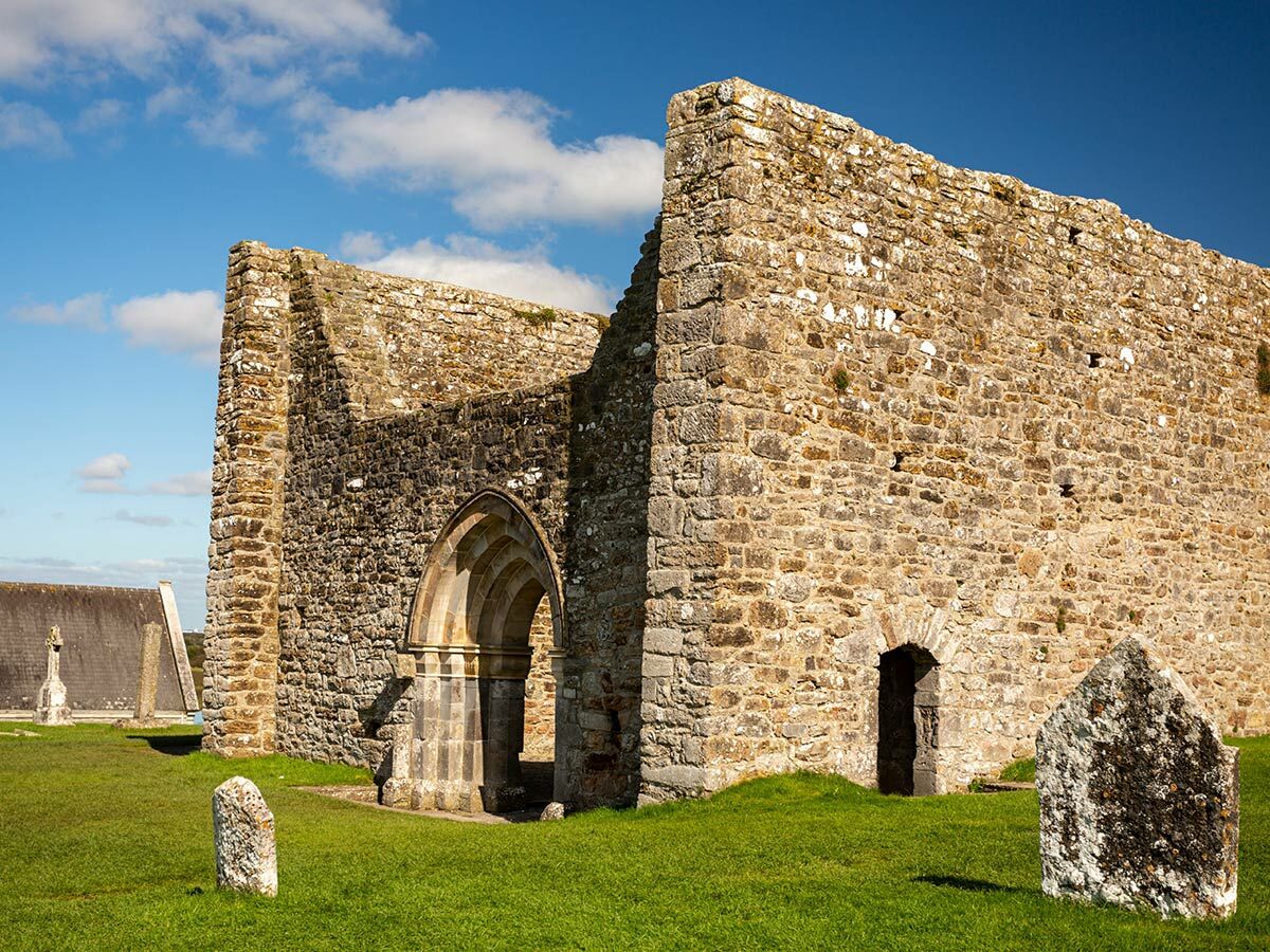 Alte Steinruine eines Klosters oder einer Kirche auf grasbewachsenem Gelände unter blauem Himmel mit weißen Wolken. Historische Stätte in Irland.