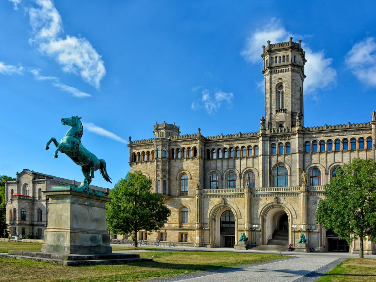 Historisches Welfenschloss der Universität Hannover mit markantem Turm und großer bronzener Pferdestatue davor unter blauem Himmel.