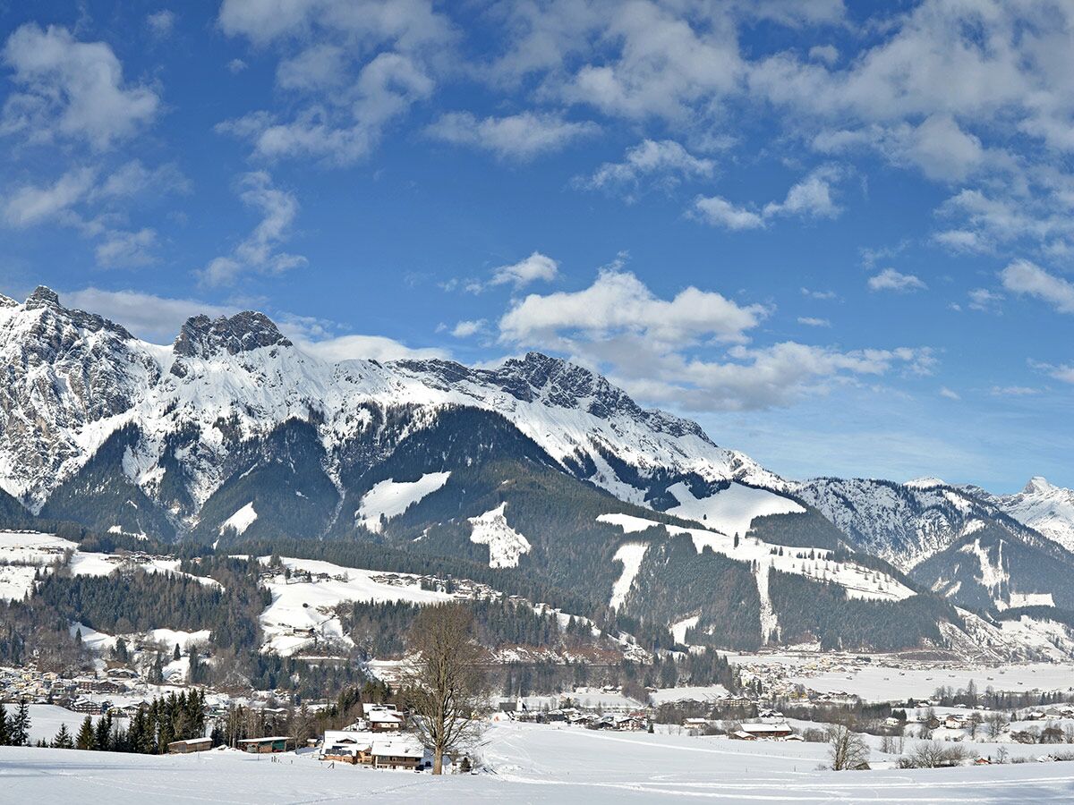 Malerische Winterlandschaft in den Alpen mit schneebedeckten Bergen, Wäldern und einem idyllischen Dorf im Tal unter blauem Himmel.