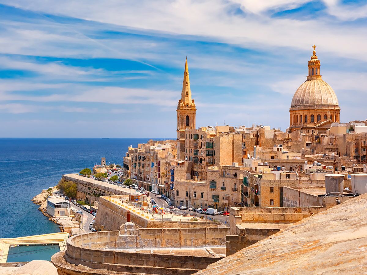 Panoramablick auf Valletta, Malta, mit historischen Gebäuden, der Karmelitenkirche, dem Meer und blauem Himmel.