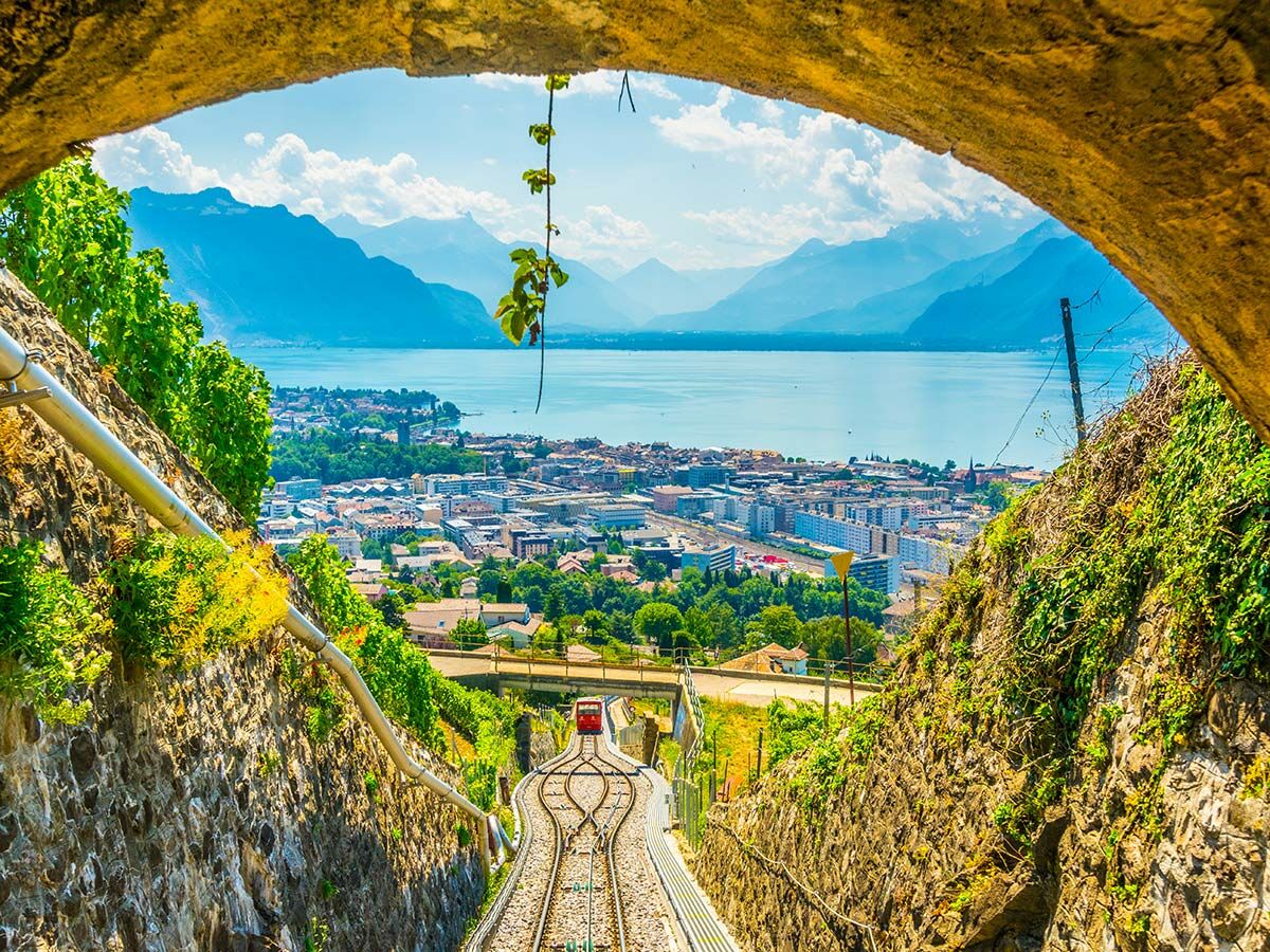 Rote Standseilbahn fährt durch einen Tunnel mit Blick auf den blauen Genfersee, eine Stadt und majestätische Alpen.