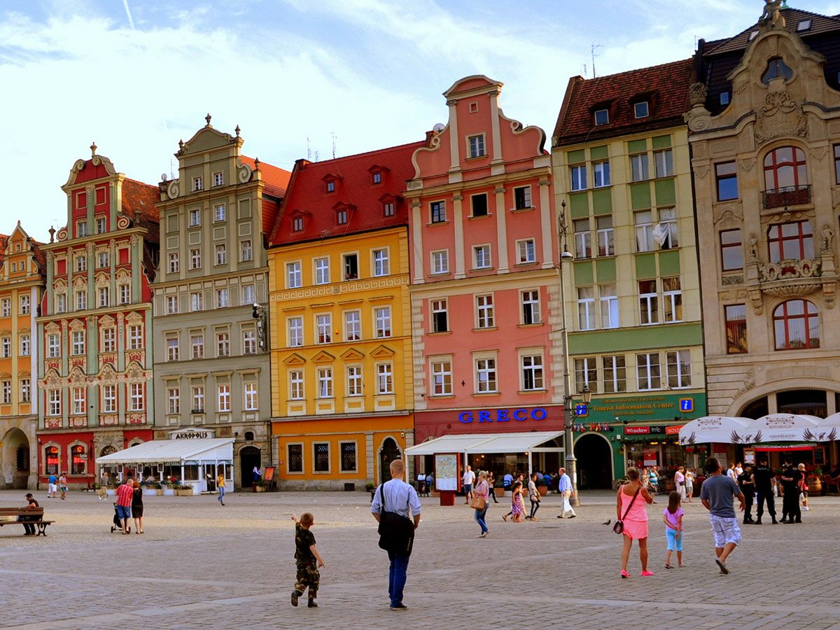 Menschen auf dem bunten historischen Marktplatz von Wrocław mit Gebäuden in Rot, Grün, Gelb und Rosa unter blauem Himmel.