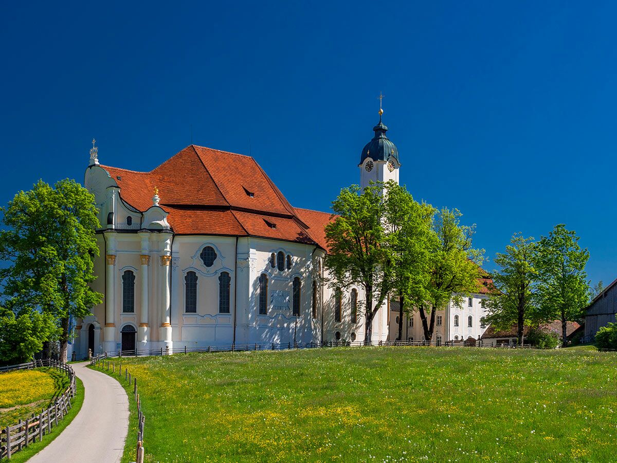 Die Wieskirche, eine Rokoko-Wallfahrtskirche in Bayern, steht unter blauem Himmel mit grünen Wiesen und Bäumen im Frühling.