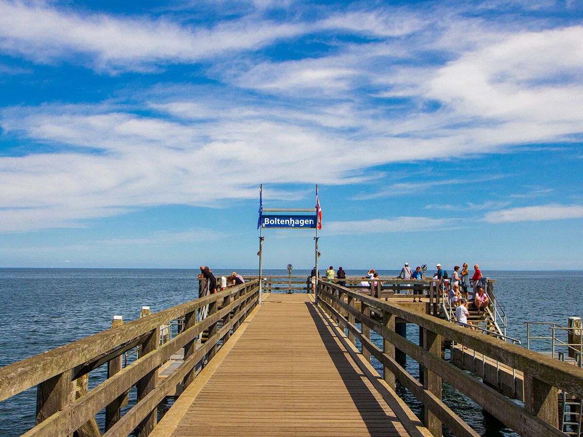 Hölzerne Seebrücke Boltenhagen mit Menschen am Meer unter blauem Himmel und weißen Wolken an der Ostseeküste.