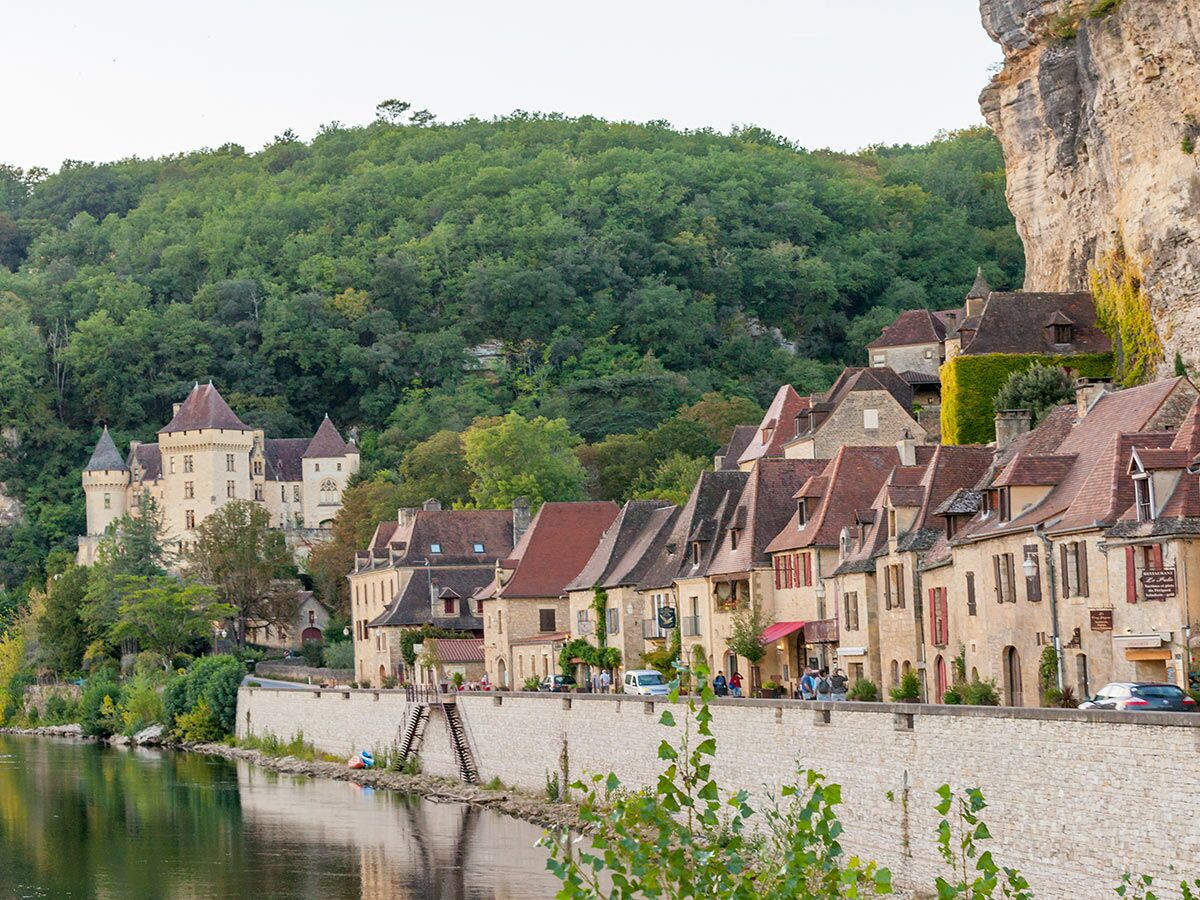 Historisches Dorf La Roque-Gageac in der Dordogne, Frankreich, mit Häusern am Fluss und Schloss an einem Felsenhang.